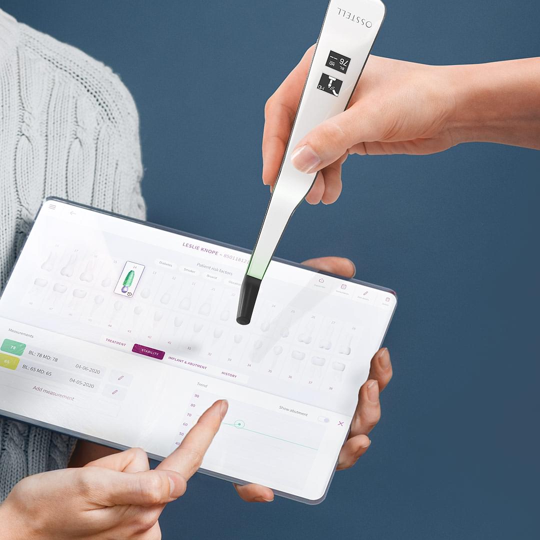 Person som håller i en iPad-liknande prototyp som visar Osstell Connect. Hand som håller i Ostells instrument som mäter stabilitet i implantat.